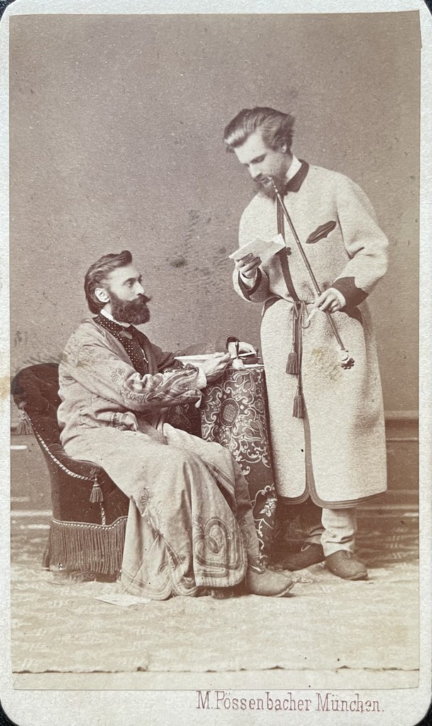 M. Pössenbacher, München, 1871. Zwei Männer in Hausmänteln. Einer davon sitzt am Tisch, während der andere eine Pfeife rauchend einen Brief liest.