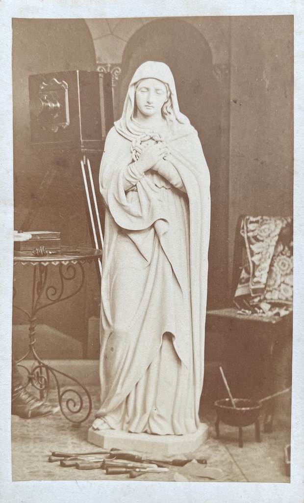 Ignaz Schwendinger, Dornbirn, ca. 1860er. Hinter einer Skulptur steht eine große Plattenkamera. Davor liegen Werkzeuge, daneben blitzt ein Fuß hervor.