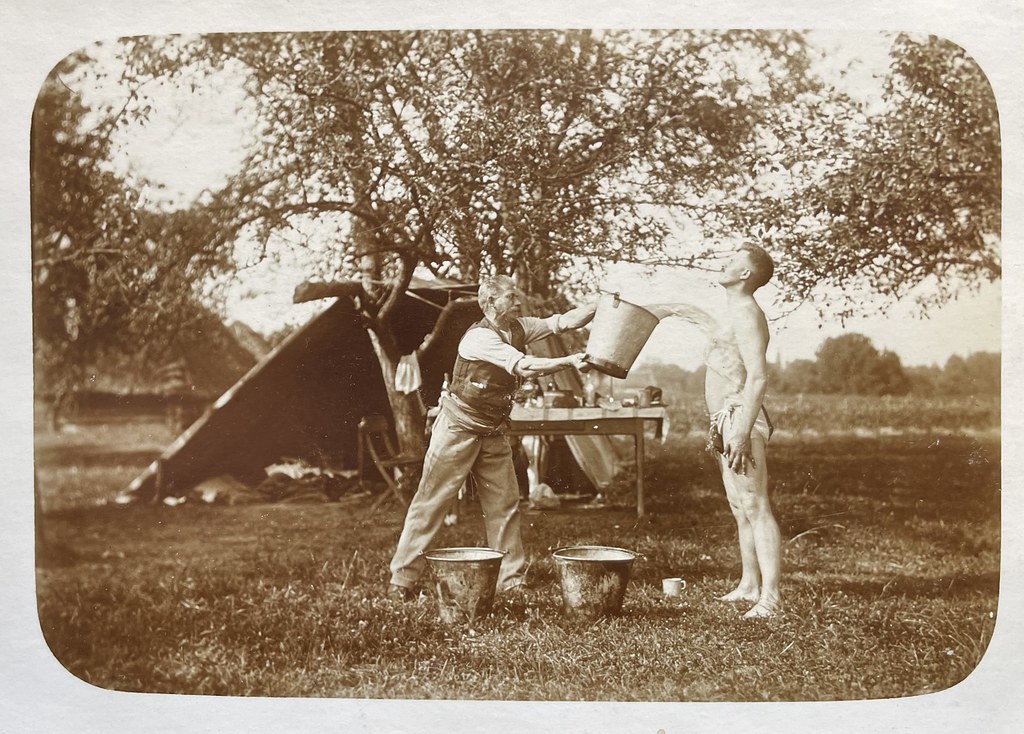 Unbekannter Fotograf, unbekannter Ort (vermutlich Österreich), ca. 1910. Ein Mann leert einem anderen, halbnackten Mann einen Kübel Wasser über den Körper.