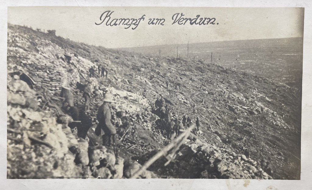 Unbekannter Fotograf, Verdun, 1916. Die Fotografie zeigt das Schlachtfeld von Verdun aus deutscher Perspektive. Im Vordergrund sieht man einen Soldaten mit Stahlhelm.